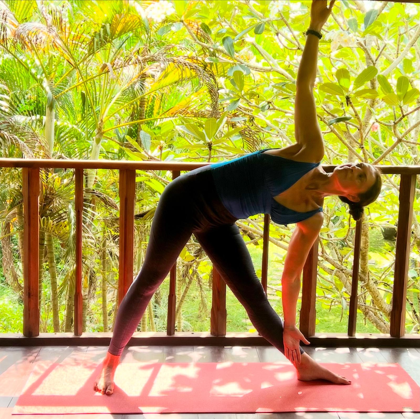 Experienced yoga teacher Alice demonstrating a strong pose in natural setting with green trees in the background